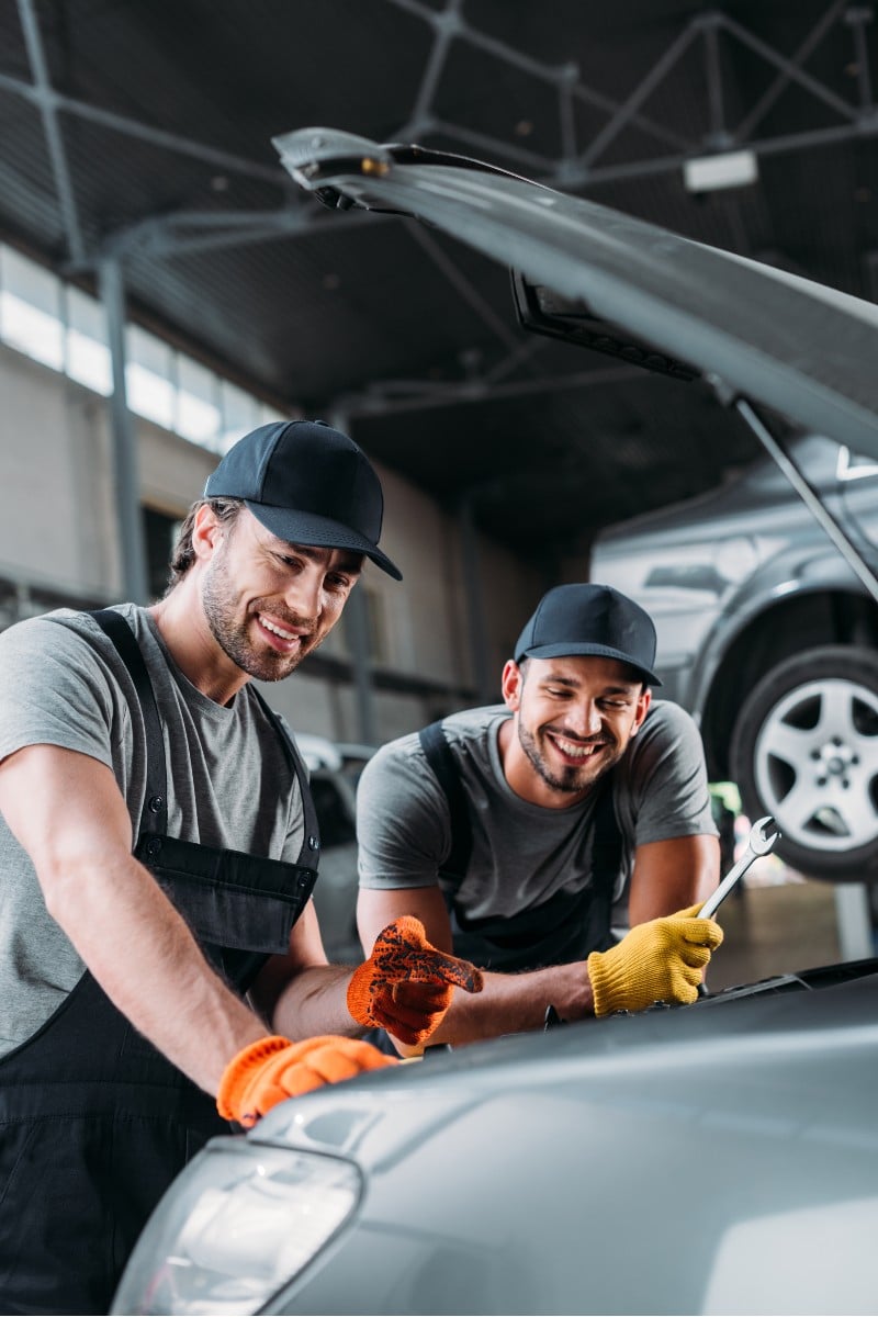 Mecânicos sorrindo observando o motor de um carro em uma oficina mecânica.